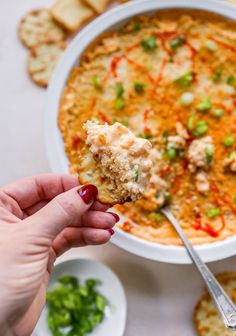 a hand holding a piece of cracker over a bowl of dip and crackers