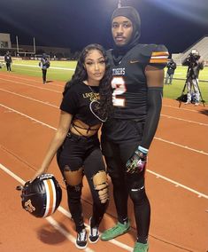 a man and woman in football uniforms posing for a photo on the field at night