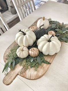 white pumpkins and greenery sit on a wooden board in front of a dining room table