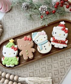 hello kitty decorated cookies are on a wooden tray next to christmas decorations and pine cones