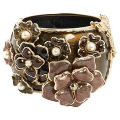 Chanel cuff bracelet in gold metal covered with brown enamel decorated with a large CC in enameled metal on one side and a large floral pattern in glass paste decorated with white rhinestones and fancy pearls, magnetic closure lined with a hook and a safety chain with carabiner, interior lined with quilted black satin. Height of the bracelet 4.65 cm (excluding floral pattern), internal diameter 5.75 cm, dimensions of the CC 4.5 x 3.5 cm, dimensions of the floral pattern 10 x 6 cm. The cuff is in Chanel Cuff Bracelet, Chanel Cuff, Satin Noir, Chanel Haute Couture, Safety Chain, Bracelet Cuff, White Rhinestone, Pearl Diamond, Magnetic Closure