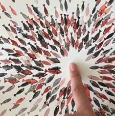 a hand is pointing at an art piece with many fish on it's surface