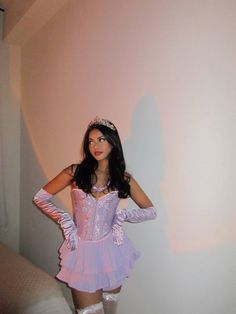 a woman in a purple dress and tiara standing next to a wall with her hands on her hips