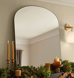 a mirror sitting on top of a mantle filled with candles and greenery next to a candle holder