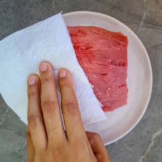 a hand is holding a piece of meat on a paper towel in front of a white plate