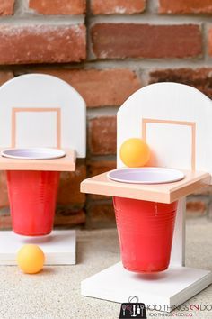 two plastic cups with oranges in them sitting on top of a white stand next to a brick wall