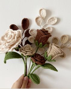 crocheted flowers are being held by someone's hand on a white wall