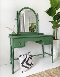 a green desk with a mirror on top and a plant in the corner next to it