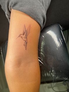 a woman's arm with a small hummingbird tattoo on the left side of her arm