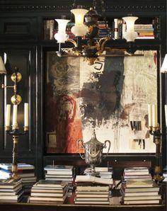 a table with many books and candles on it in front of a wall full of pictures