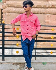 a man in pink shirt and blue jeans standing next to a fence