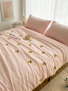 a bed with pink sheets and yellow lemons on it, next to a window