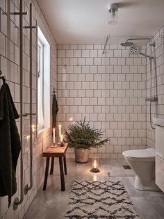 a white tiled bathroom with candles on the floor and a potted plant in the corner