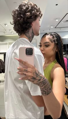 a man and woman standing in front of a mirror looking at their cell phones together