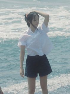 a woman standing on top of a beach next to the ocean with her head in her hands