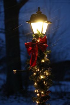 a street light decorated with christmas lights and a red bow hanging from it's side