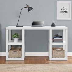 a white desk with two baskets on it and a lamp next to it in front of a gray wall