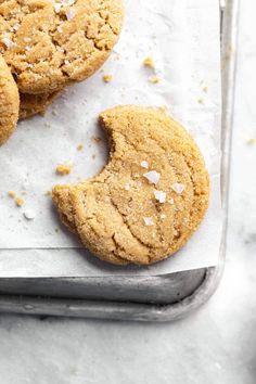 three cookies on a baking sheet with one cookie broken in half and the other whole