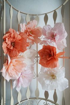 pink and white paper flowers are hanging from a metal rack in front of a window