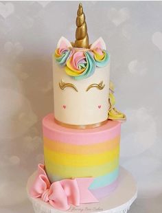 there is a rainbow cake with a unicorn on top and a pink bow at the bottom