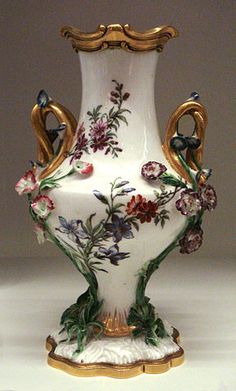 a white vase with flowers painted on the side and gold trimming around the bottom