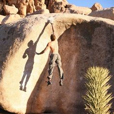 a man climbing up the side of a large rock with his hands in the air