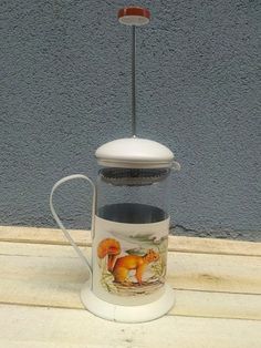 a coffee pot with a handle on top of a wooden table next to a wall