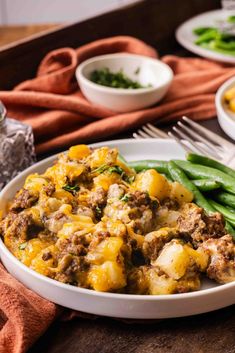 a white plate topped with green beans and potatoes next to other plates filled with food