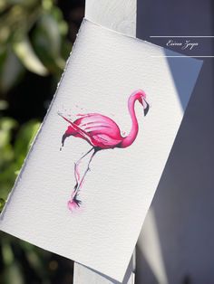 a painting of a pink flamingo on a white piece of paper hanging from a wooden post