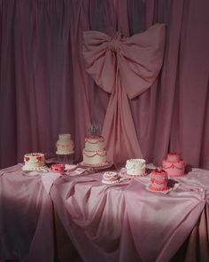 a table topped with lots of cakes and cupcakes on top of pink cloth