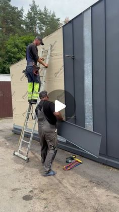 two men are painting the side of a building with paint rollers and ladders