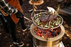 a person standing next to a grill filled with meat and vegetables on top of it