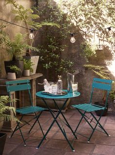 two green chairs sitting on top of a patio next to a small table and potted plants