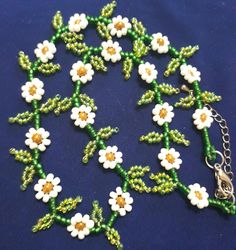 a green and white beaded necklace with flowers on the front, sitting on a blue surface