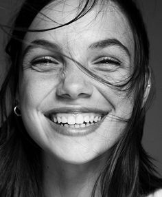 a black and white photo of a smiling woman with her hair blowing in the wind