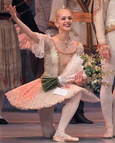 a ballerina is sitting on the floor with her arms in the air while holding flowers