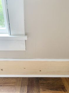 the corner of a room with wood flooring next to a window and white trim