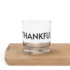 a glass with the words thankful on it sitting on top of a wooden tray