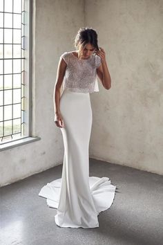 a woman in a white wedding dress standing by a window with her hand on her head