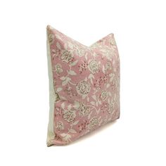 a pink and white pillow with floral print on it's side, sitting against a white background