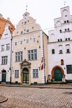 a cobblestone street lined with white buildings and green doors in the middle of town