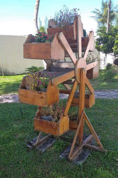 a wooden wheel with plants growing out of it in the grass next to a building