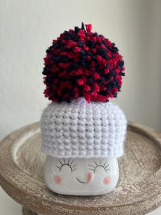 a crocheted hat on top of a white cup with red and blue pom - poms