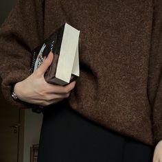 a woman is holding a piece of paper in her hand while wearing a brown sweater