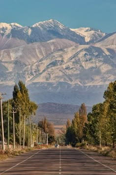 an empty road with mountains in the background and snow on the top of the mountain