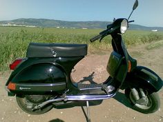 a black scooter parked on the side of a dirt road next to a field