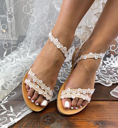 a bride's feet wearing sandals with lace and flowers on them, while standing on a wooden platform