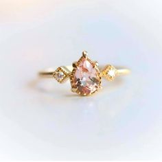 an engagement ring with a pink stone and two white stones on the side, set in yellow gold