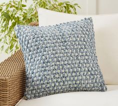 a blue and white pillow sitting on top of a couch next to a wicker basket