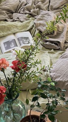 two vases filled with flowers on top of a bed next to an open book